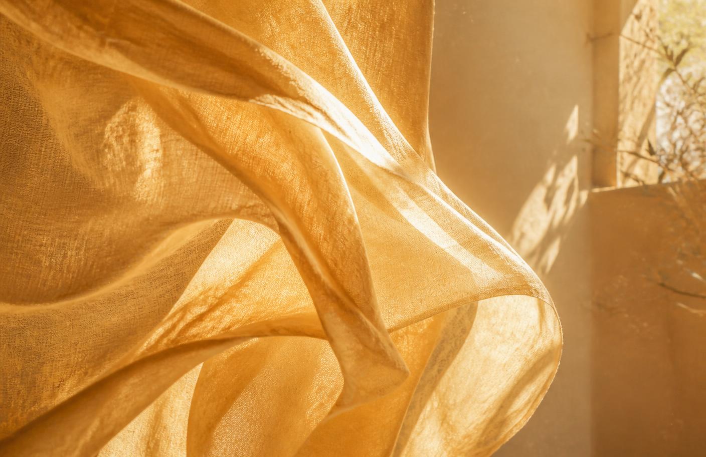 Sheer golden silk lifting in soft light beside a sunlit window — the tender, translucent nature of emotional truth.